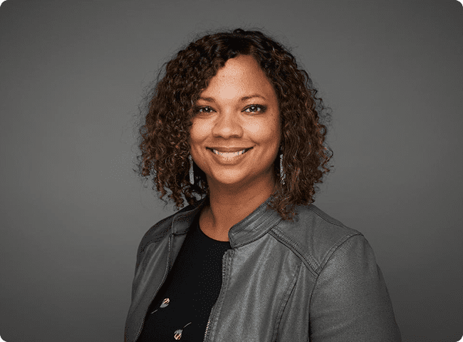 Smiling woman with curly hair and jacket.